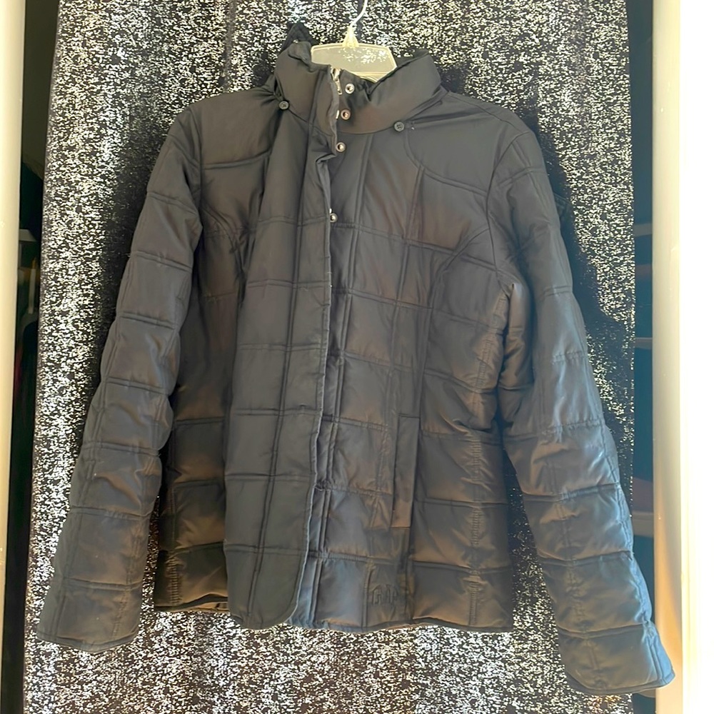 A black puffy coat with two pockets, a zipper, buttons in the front and a hood.